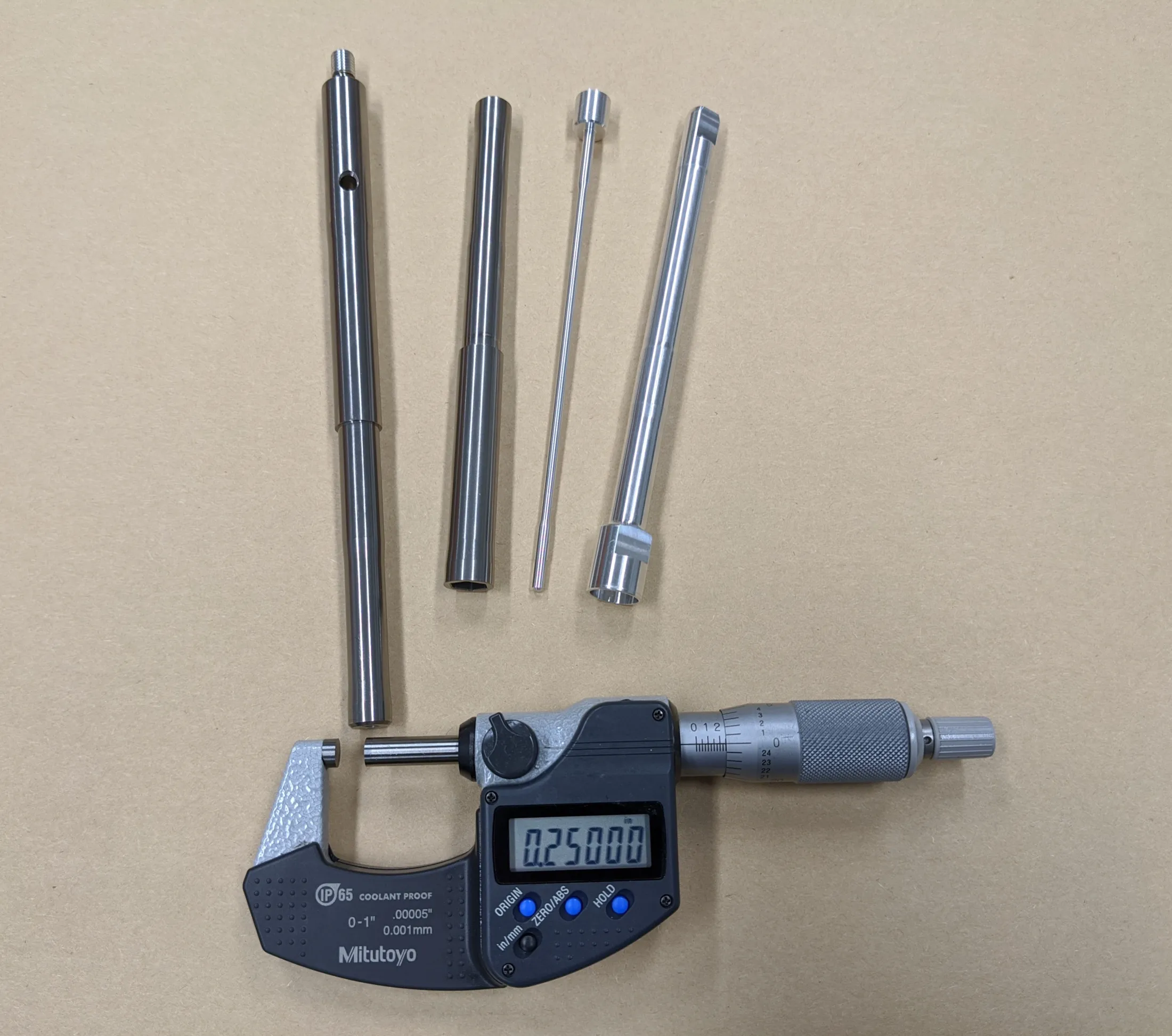 A Mitutoyo digital micrometer reading 0.25000 inches beside four turned parts