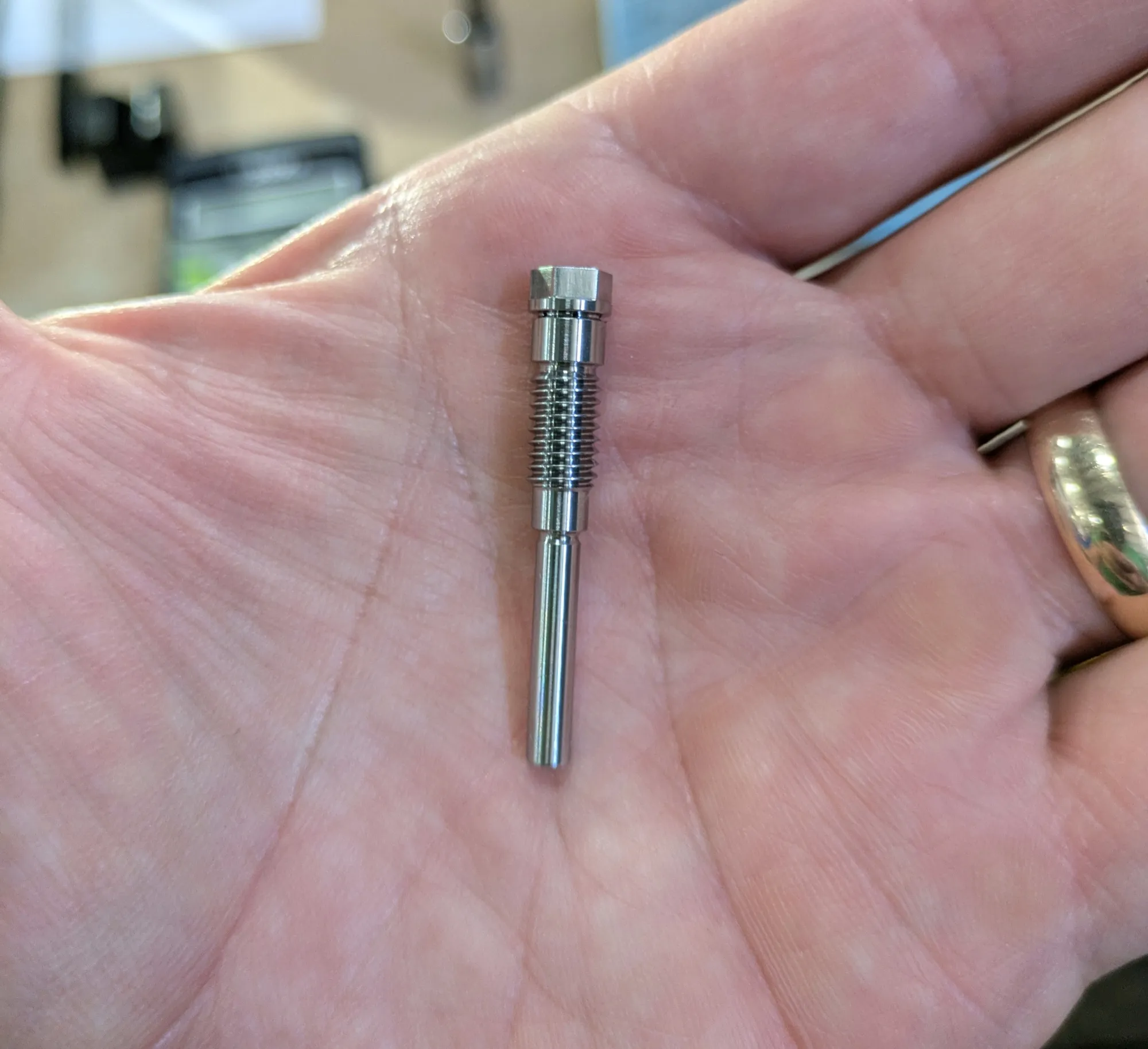 A small threaded Swiss-turned stainless pin held in the palm of a hand for scale